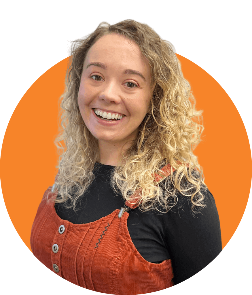 Charlotte Speaight smiling in a burnt orange dungarees dress against an orange circle backdrop