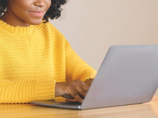 Women in yellow knitted jumper typing away at her desktop laptop