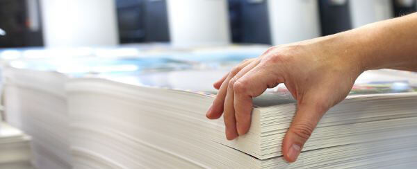 A person holding a stack of freshly digitally printed paper.
