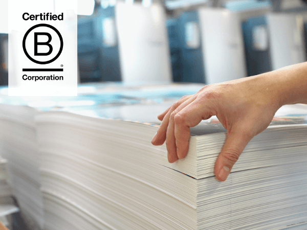 A person proudly flicks through a stack of printed materials, showcasing their B Corp Certification as a printer and mailing house business