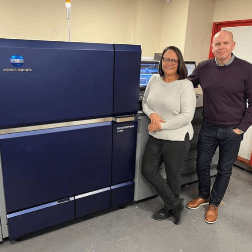Lance Hill MD and Karen Herbert Operations Director standing in front of a large Konica Minolta digital press